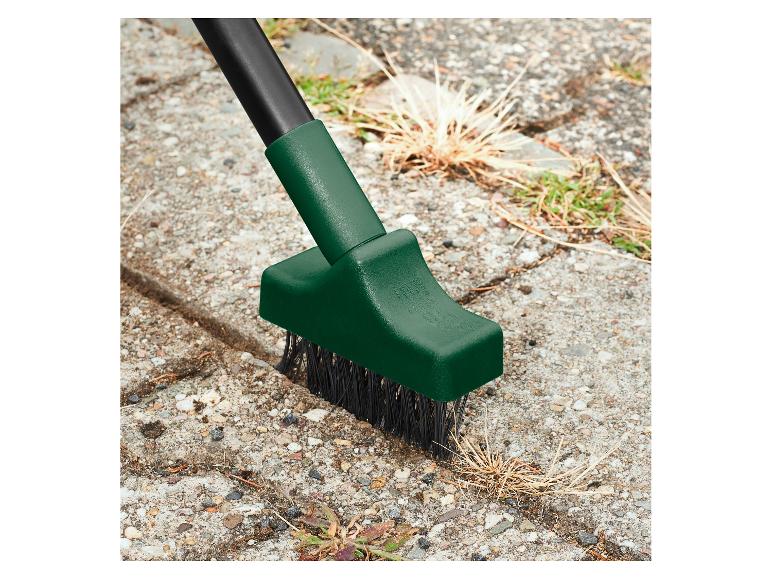 Brosse à désherber avec un long manche, nettoyant les mauvaises herbes entre les pavés.