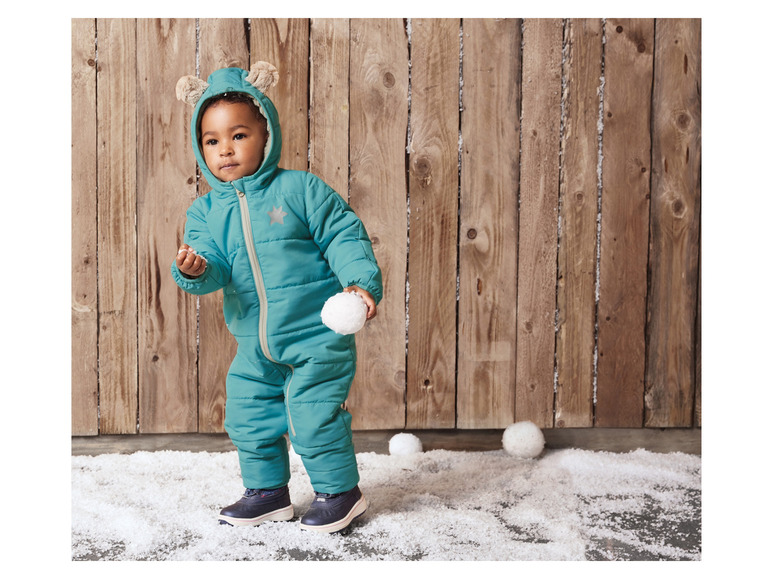 Un enfant portant une combinaison d'hiver verte avec des oreilles joue avec des boules de neige.