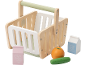 Panier de courses en bois avec aliments jouets : lait, jus de raisin, orange et concombre.