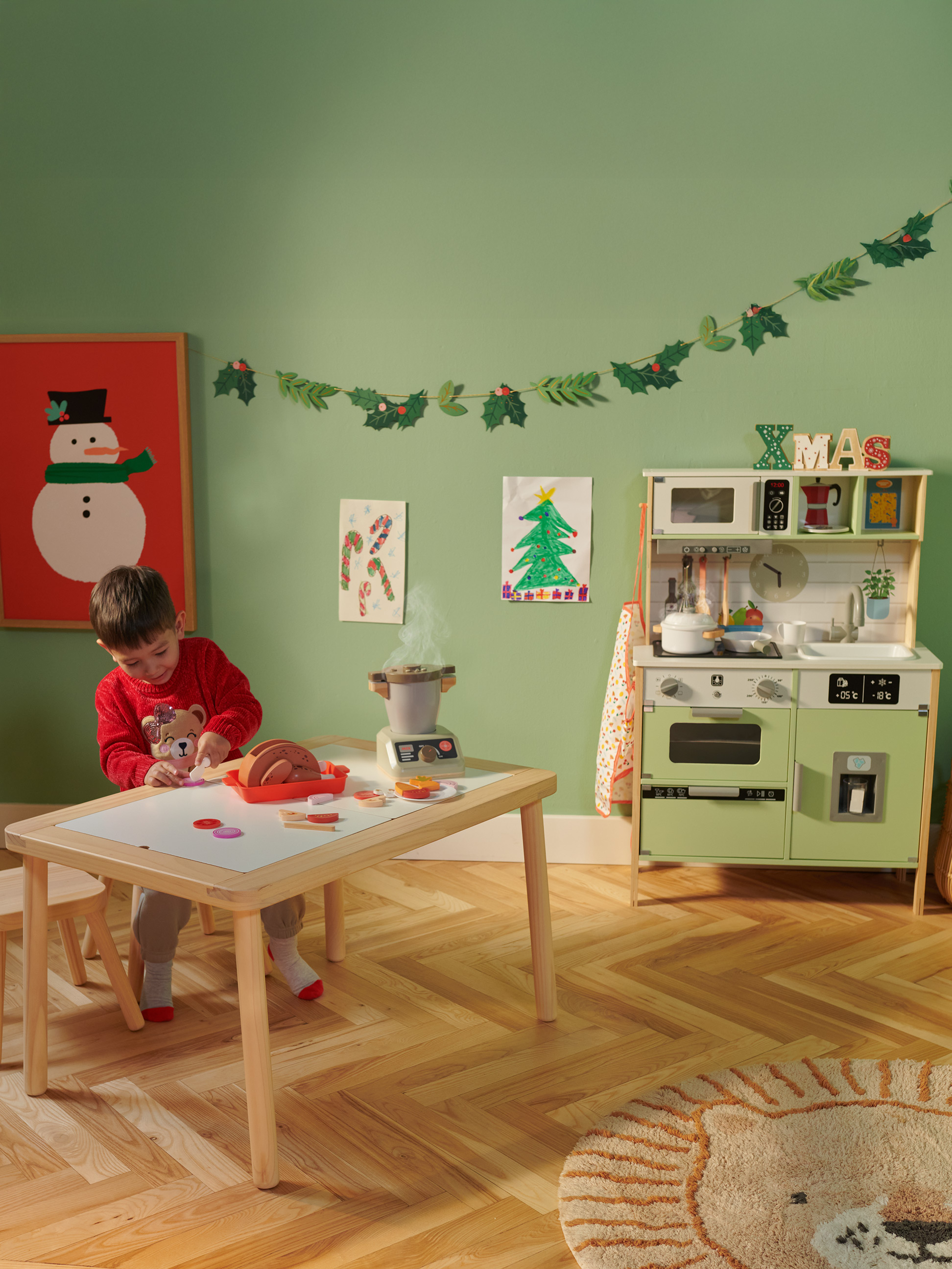Un enfant joue avec une cuisine et une table à manger dans une pièce décorée pour Noël.