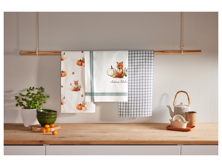 Serviettes de cuisine à motifs de citrouilles et de renards, une théière et des bols sur un comptoir en bois.