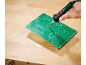 Une main soude une carte de circuit imprimé verte sur un établi en bois.