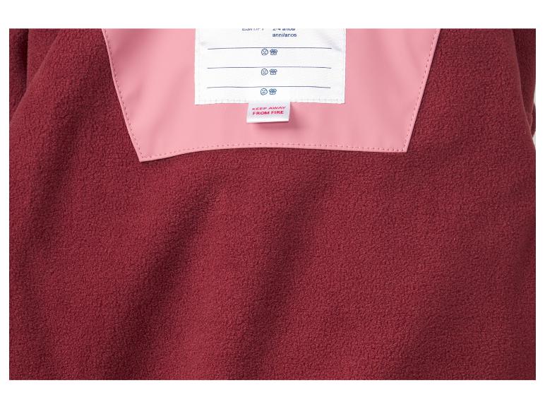 Gros plan d'un vêtement en polaire rouge avec doublure rose et étiquette 'Tenir à l'écart du feu'.