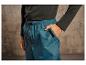 Un homme porte un t-shirt vert foncé et un pantalon de survêtement bleu imperméable.
