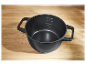Une casserole foncée avec des poignées sur une surface en bois.