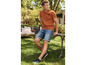 Homme portant un t-shirt orange et un short en jean bleu assis sur un banc en bois dans le jardin.