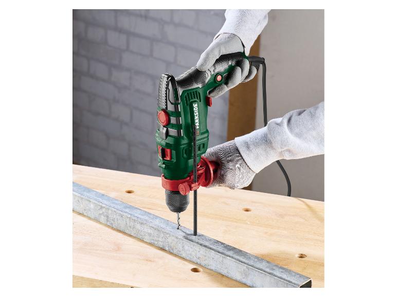 Perceuse à percussion dans les mains, perçant un profil métallique sur une table en bois.