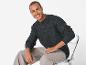 Un homme portant un pull gris foncé et un pantalon beige assis sur une chaise.