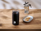 Moulin à café noir avec grains, cafetière moka et biscuits sur une table en bois.