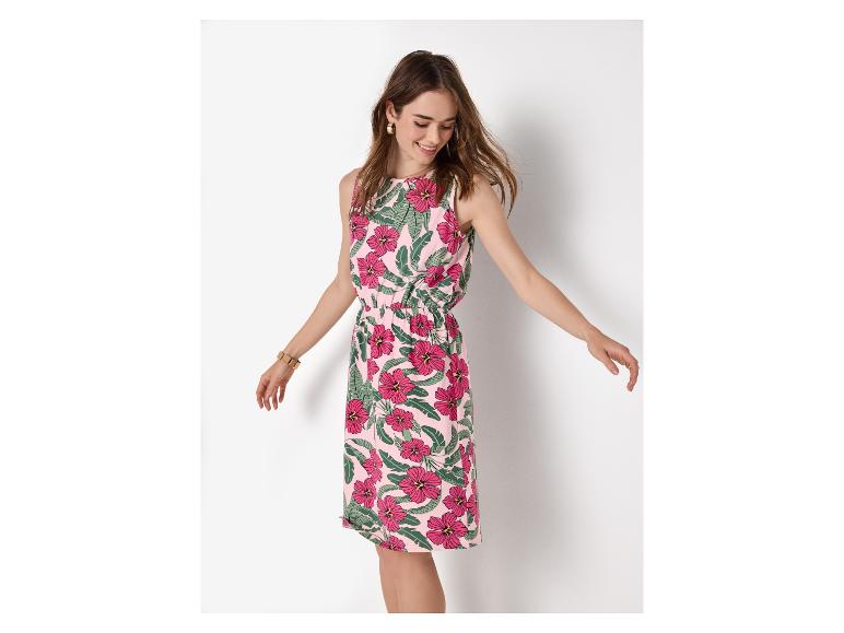 Femme en robe d'été rose fleurie avec des feuilles vertes, souriante et regardant vers le bas.