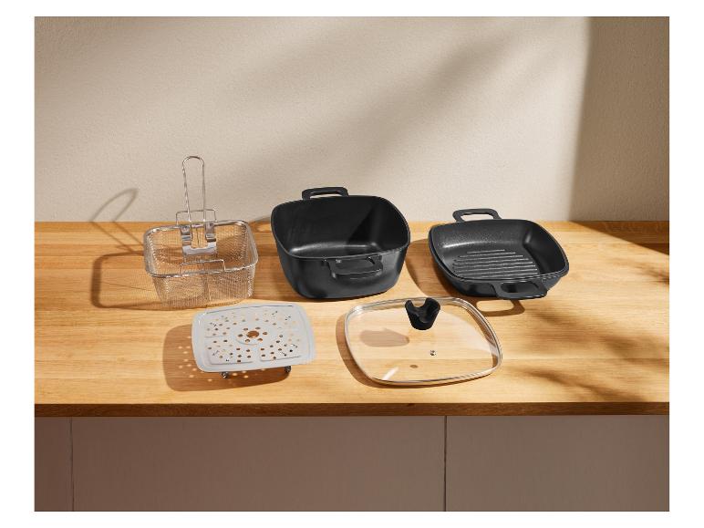 Un ensemble de casseroles carrées noires, un panier à friture métallique, un insert vapeur et un couvercle en verre sur un comptoir en bois.