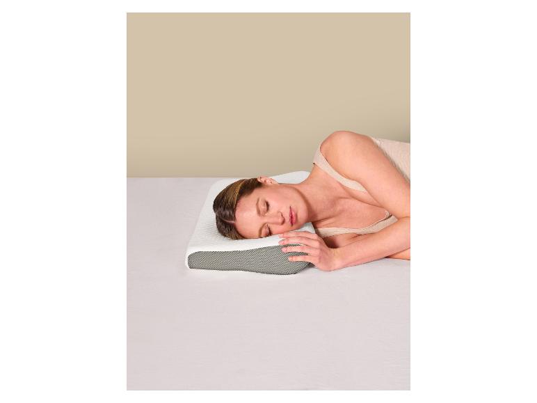 Femme dormant sur le côté sur un oreiller ergonomique dans un lit aux draps blancs.
