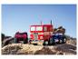 Un camion jouet Optimus Prime et une télécommande sur un terrain rocheux sous un ciel clair.