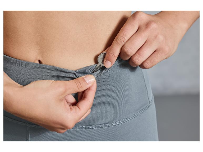 Une femme met une clé dans la poche d'un legging gris.