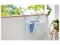 Un étendoir blanc avec des vêtements bleus et verts, fixé à une rambarde de balcon.
