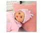 Une poupée en pyjama et bonnet roses avec des cœurs et des roses, allongée sur un coussin rose.