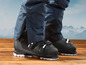 Des chaussures de ski avec un pantalon de ski bleu sur fond de montagnes.