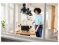 Femme nettoyant un ordinateur portable avec un aspirateur à main sur une table en bois dans une pièce lumineuse.