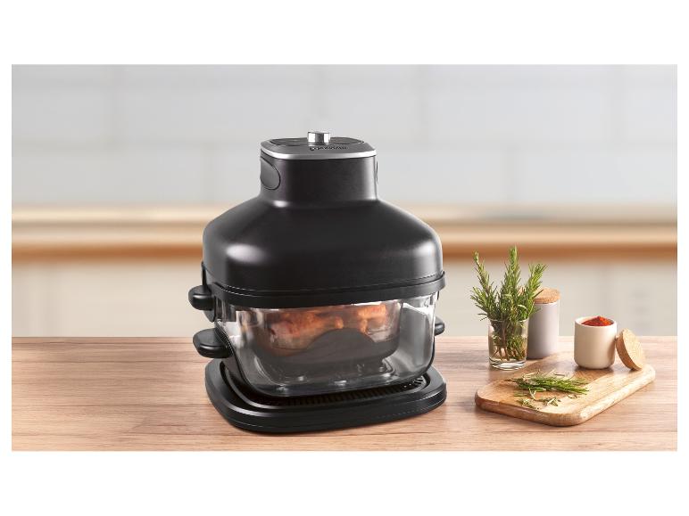 Friteuse à air noire avec des aliments à l'intérieur, sur une table en bois avec des herbes et des épices.
