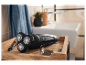 Un rasoir électrique à trois têtes repose sur un plateau en bois dans une salle de bain.