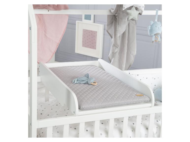 Table à langer blanche avec matelas gris, placée au-dessus d'un lit bébé.