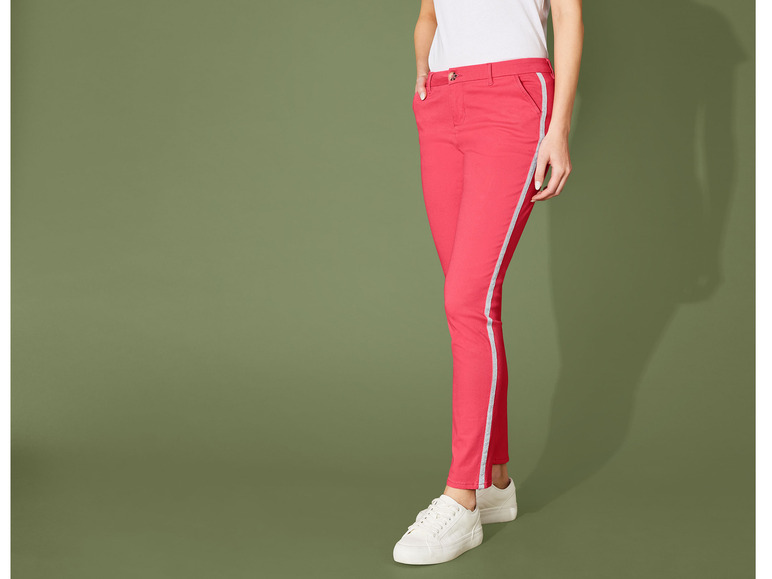 Une femme porte un pantalon rose avec des bandes blanches et des baskets blanches.