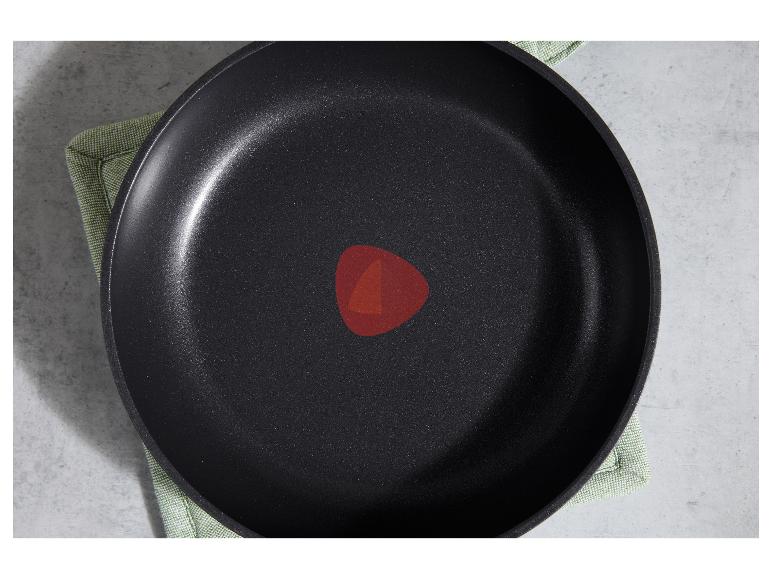 Poêle noire avec revêtement antiadhésif et indicateur de température rouge sur une surface grise.