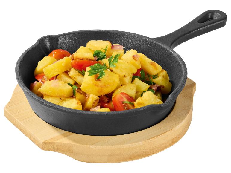 Pommes de terre sautées avec tomates, oignons et persil dans une poêle en fonte sur un support en bois.