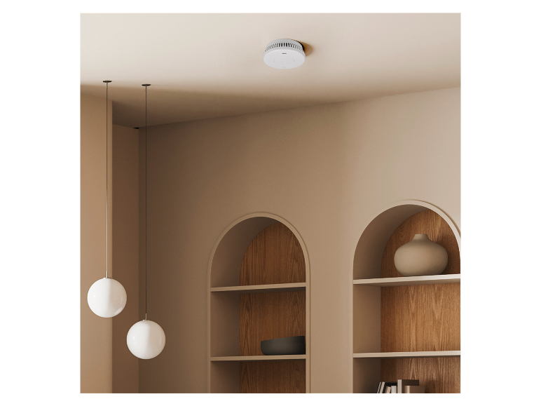 Détecteur de fumée sur un plafond clair avec niches décoratives et lampes suspendues.