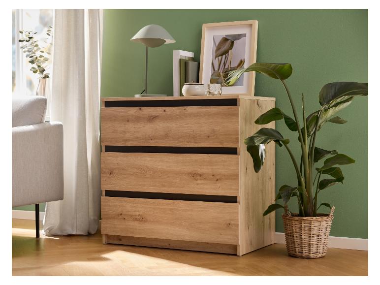 Commode en bois à trois tiroirs, à côté d'un canapé, de rideaux et de plantes.