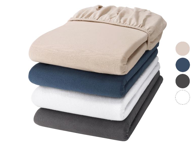 Pile de quatre draps-housses unis en beige, bleu, blanc et gris foncé.
