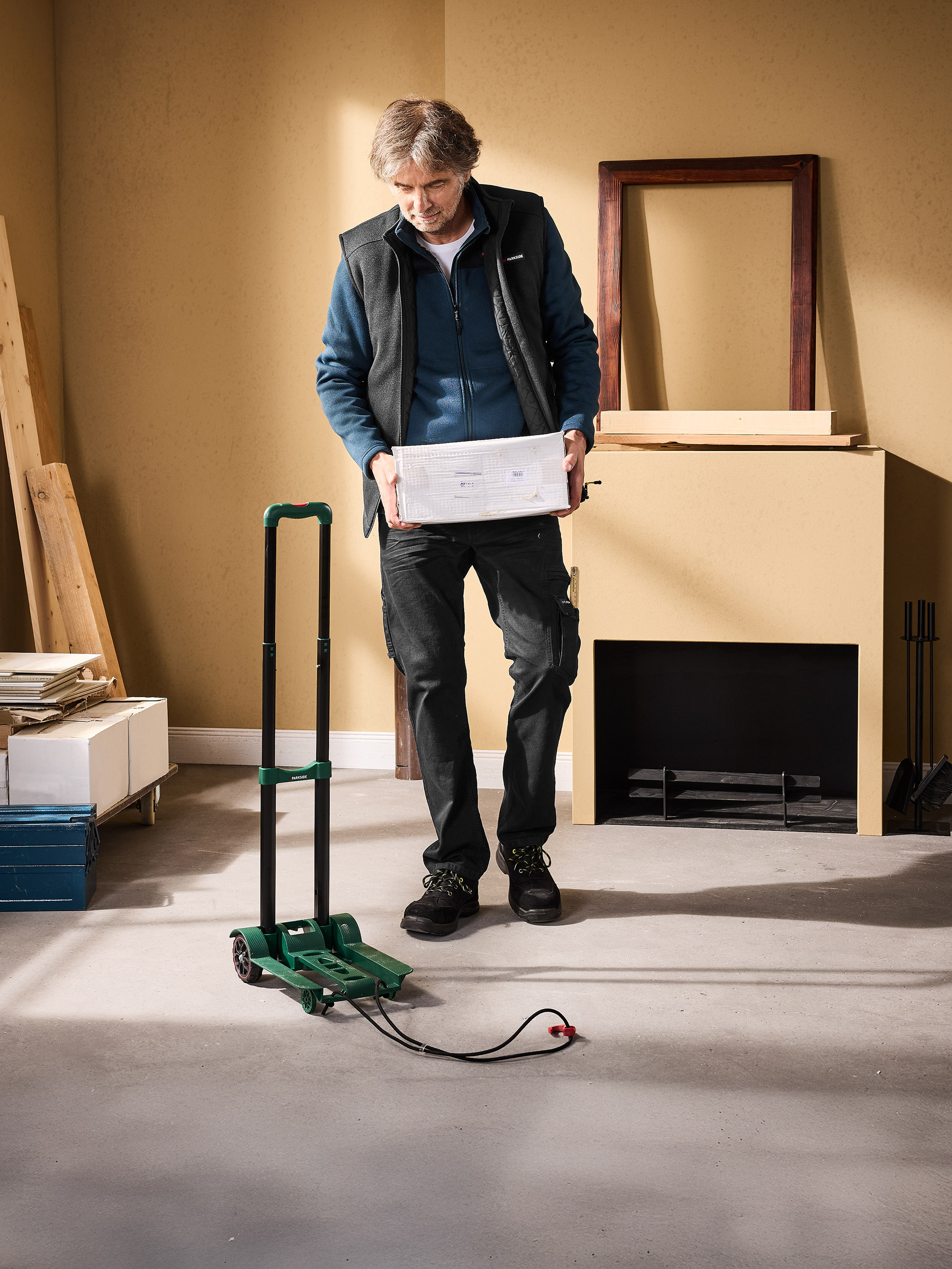Homme tenant une boîte blanche, à côté d'un chariot vert et d'une cheminée.