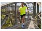 Un homme court sur un pont, vêtu d'un t-shirt jaune et de chaussures de course bleues.