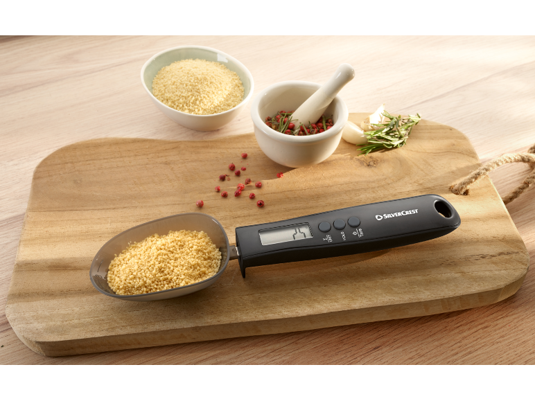 Cuillère doseuse numérique avec du couscous sur une planche en bois avec des épices