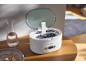 Nettoyeur à ultrasons avec lunettes sur une table en bois, à côté d'une carafe et de bijoux.