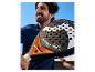 Homme souriant tenant une raquette de padel avec des détails orange et le texte « X STEFANIE GRAF ».