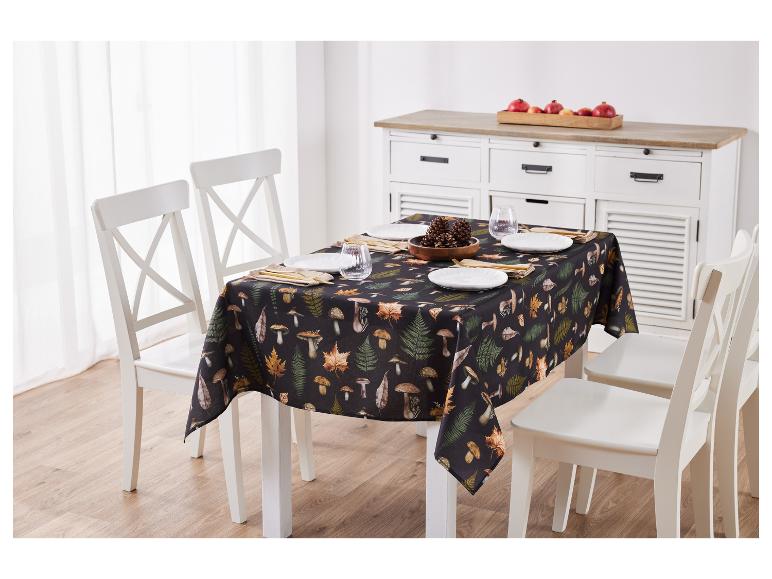 Image d'une table avec une nappe d'automne à motifs de champignons et de feuilles, et des chaises blanches.