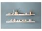 Deux étagères blanches présentant divers objets décoratifs comme des vases, des bougies et un arrosoir doré sur un mur bleu.