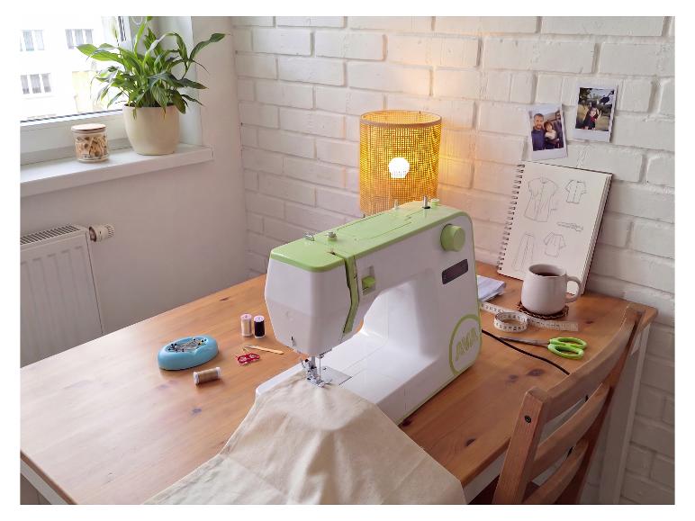 Machine à coudre sur un bureau en bois avec fournitures de couture, une plante et une lampe.