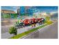 Un train jouet rouge Lego City à une gare, avec des figurines et des bâtiments en arrière-plan.