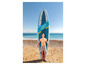 Un homme pose avec une planche de paddle gonflable Hydro-Force sur une plage de sable.