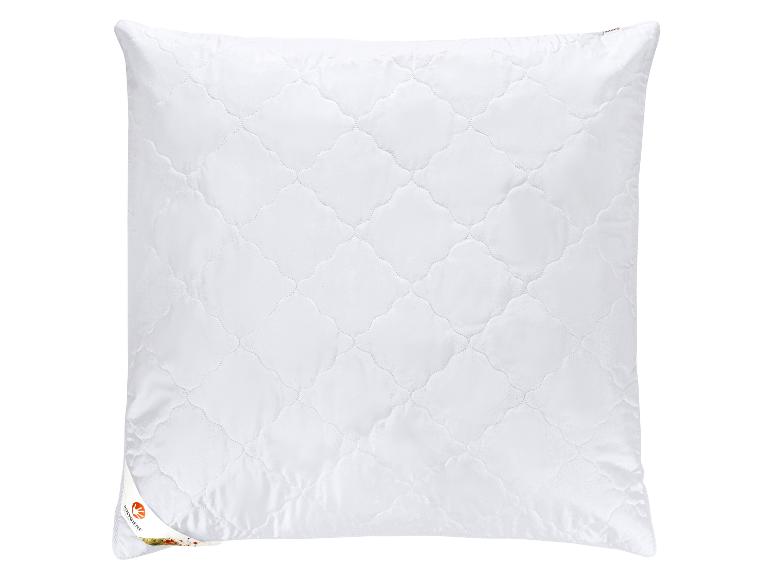 Oreiller blanc matelassé avec un motif de losanges et une petite étiquette dans le coin inférieur gauche.