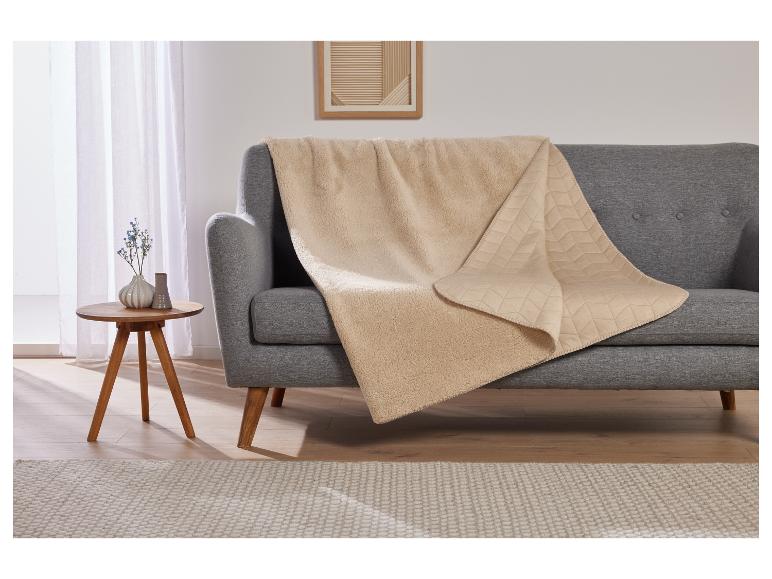 Une couverture beige avec une texture de sherpa sur un canapé gris.