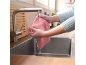 Femme rinçant un chiffon en microfibre rose sous un robinet de cuisine en acier inoxydable.