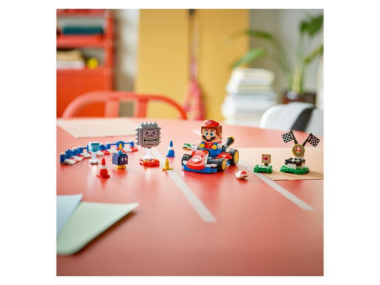 Ensemble de jeu avec figurine de personnage en kart, obstacles et ligne d'arrivée sur une table rouge.