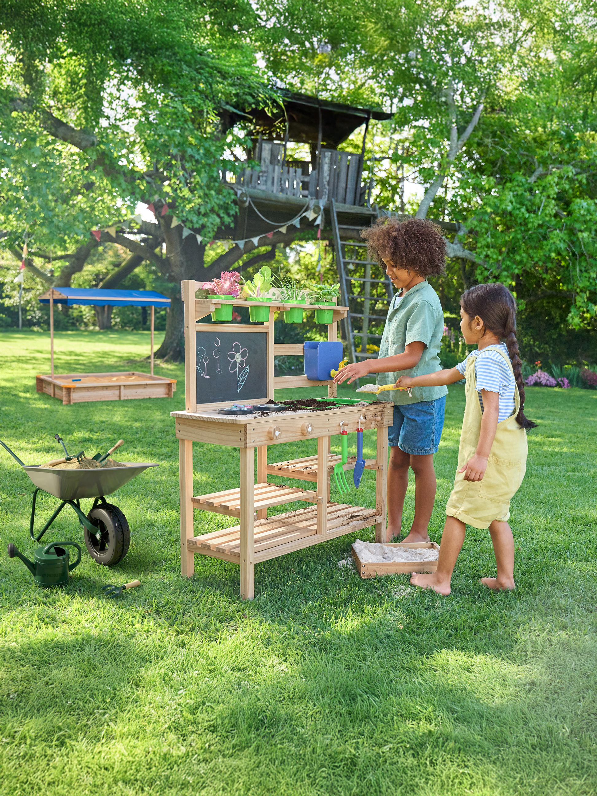 Enfants jouant avec une table de jardinage et un bac à sable dans le jardin.