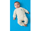Bébé en pyjama clair avec un ours brodé, allongé sur un fond bleu.