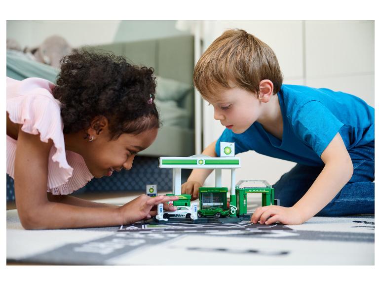 Deux enfants jouent sur le sol avec un ensemble de jeu BP, incluant une station-service.