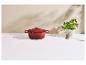 Cocotte en fonte rouge sur un comptoir blanc avec du basilic et des piments séchés.