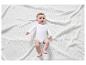 Un bébé allongé sur une couverture blanche portant un body blanc avec un imprimé rose.